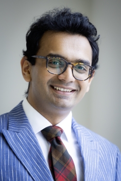 Man wearing glasses in blue pinstripe suite and red checkered tie smiling