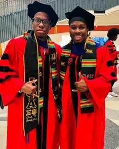 Two men in red graduation robes and black caps standing and smiling