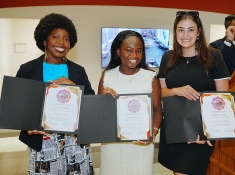 Three women smiling and holding up certificates
