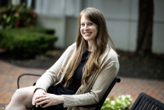 woman with long hair smiling and sitting on outdoor bench