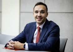 man in blue suit and tie smiling with hands folded at table