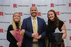 man standing in the middle of two women and smiling in front of Rutgers Law background