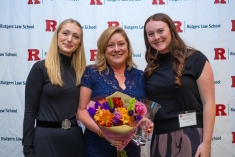 three women standing next to each other and smiling in front of Rutgers Law background