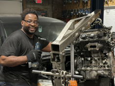 man smiling in all black working on machine in auto garage