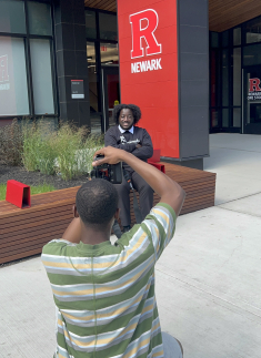 man kneeling down taking picture of seated man outdoors