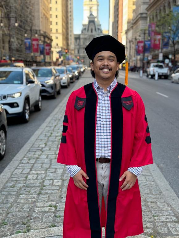man smiling and standing on Philadelphia street with hood and graduation cap