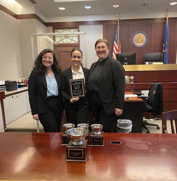 Three women in courtroom smiling and posing with trophies