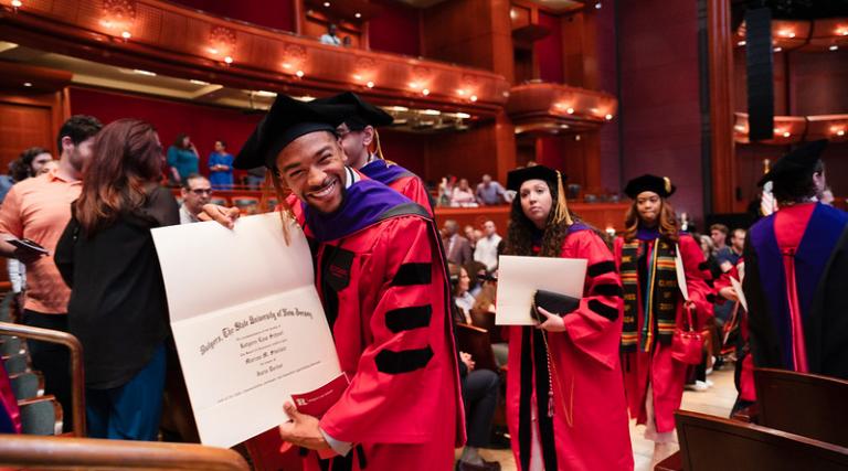 man in red robe holding degree and smiling