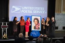 women on stage clapping after reveal large postage stamp