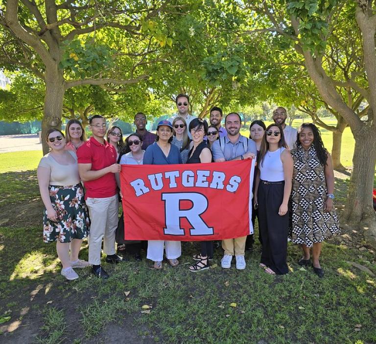 group of people holding Rutgers banner under tree in park