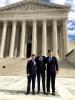 Three law students stand in front of the U.S. Supreme Court in the sun.
